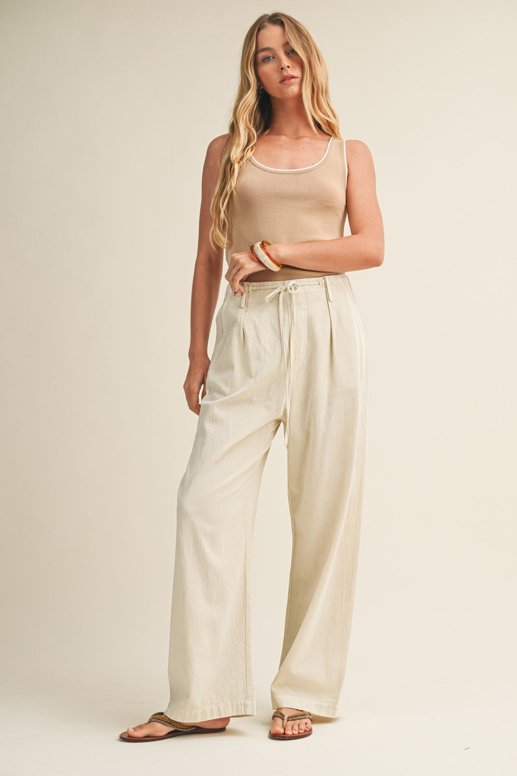 Woman wearing a latte knit tank top and pants against a beige background