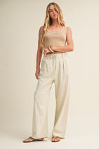 Woman wearing a latte knit tank top and pants against a beige background