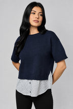 Woman wearing a blue knit short sleeve sweater with checkered shirt tail against a taupe background