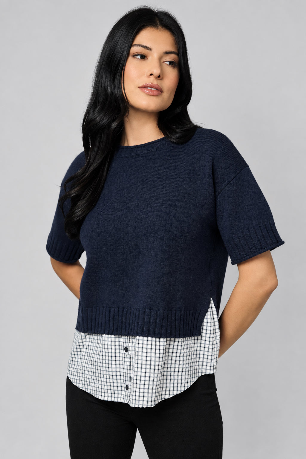 Woman wearing a blue knit short sleeve sweater with checkered shirt tail against a taupe background