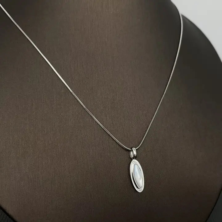 Silver necklace with a shell inlaid pendant on a brown surface