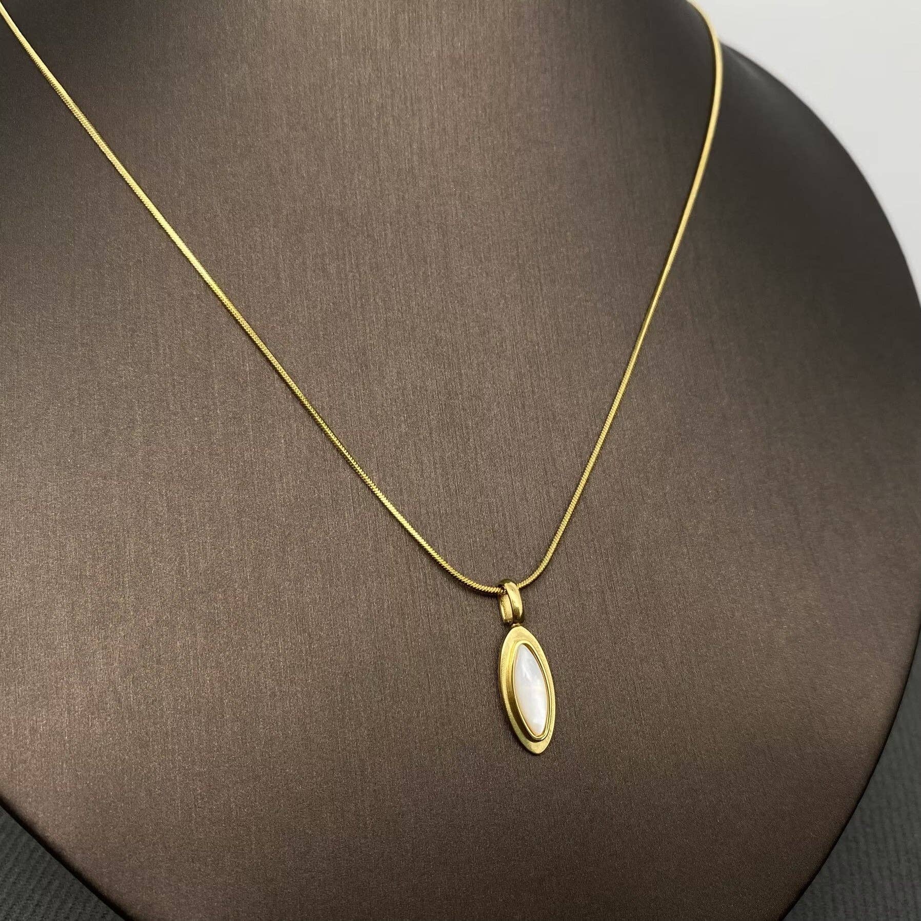 18k gold-plated necklace with a inlaid shell pendant on a brown surface
