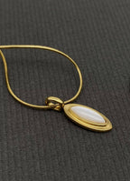 Close up of 18k gold-plated necklace with a inlaid shell pendant on a gray surface