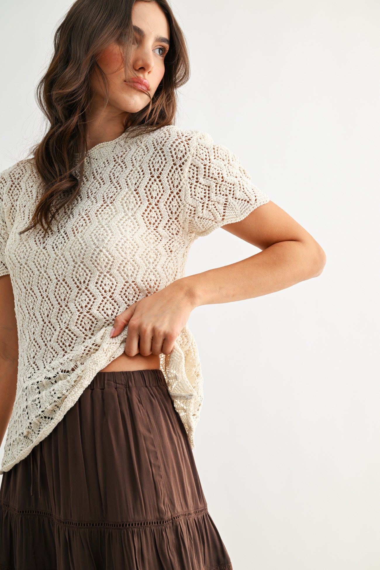 Woman wearing a cream lace top and brown skirt on a white background