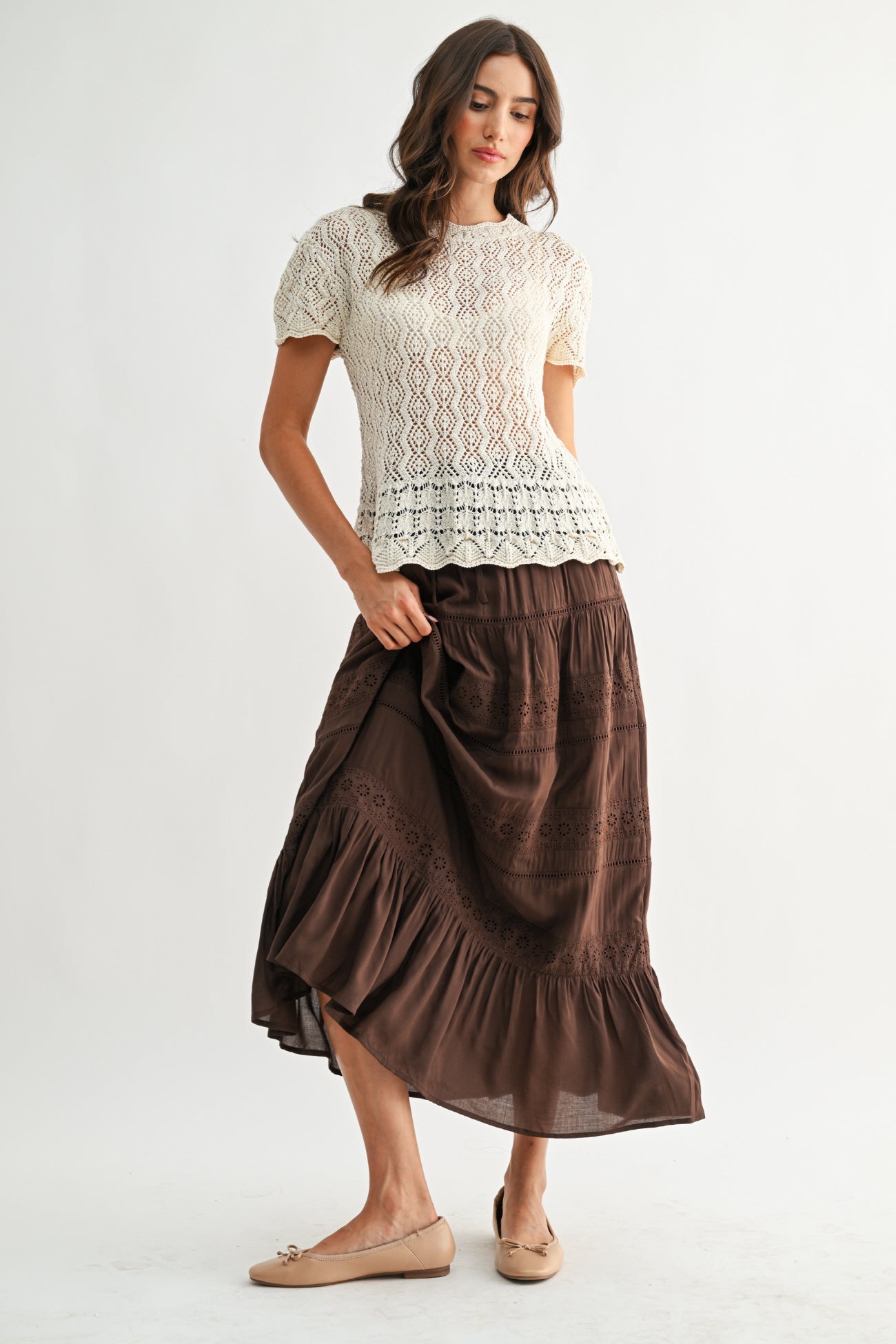 Woman wearing a cream lace top and brown skirt on a white background