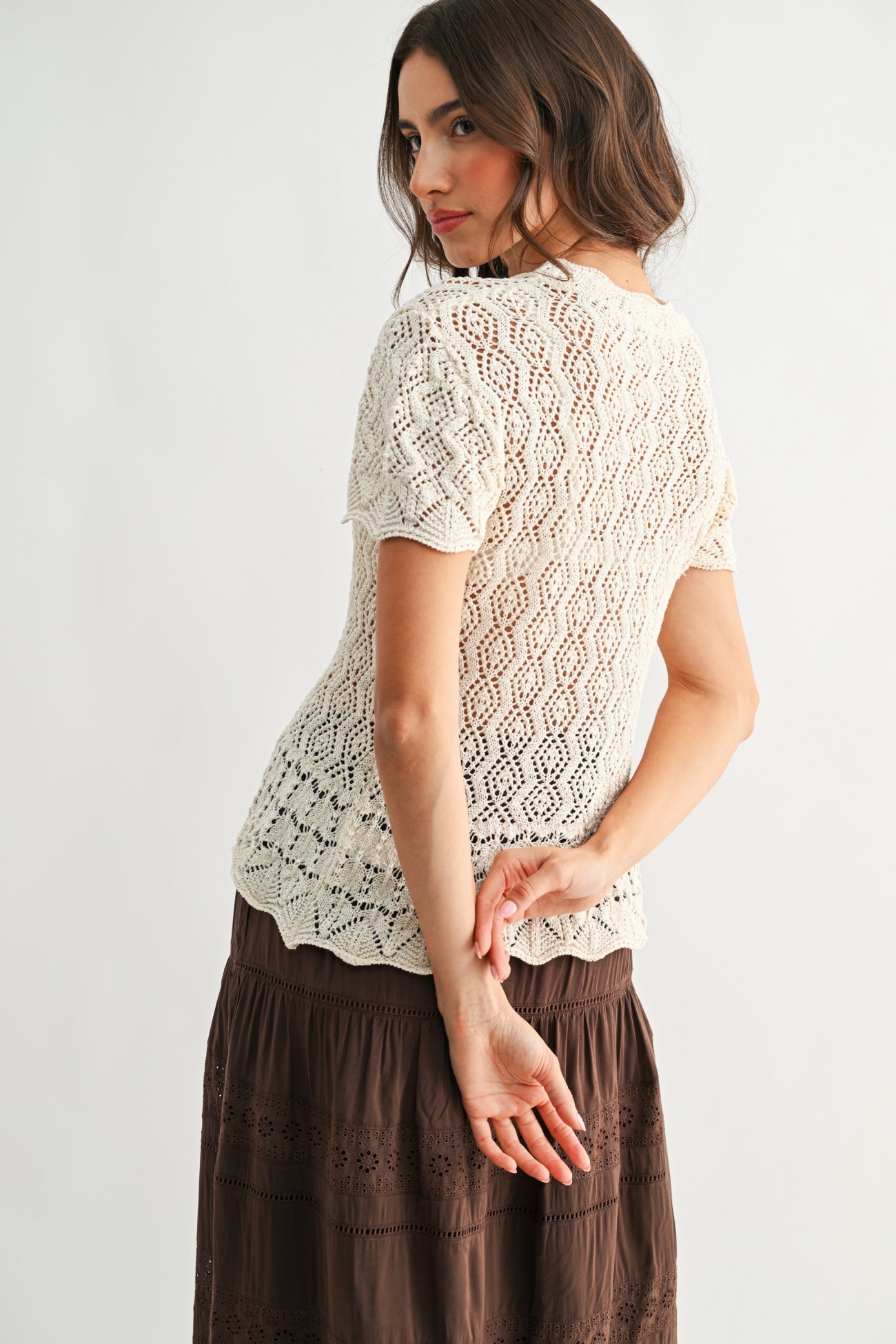 Back view of a woman wearing a cream lace top and brown skirt on a white background