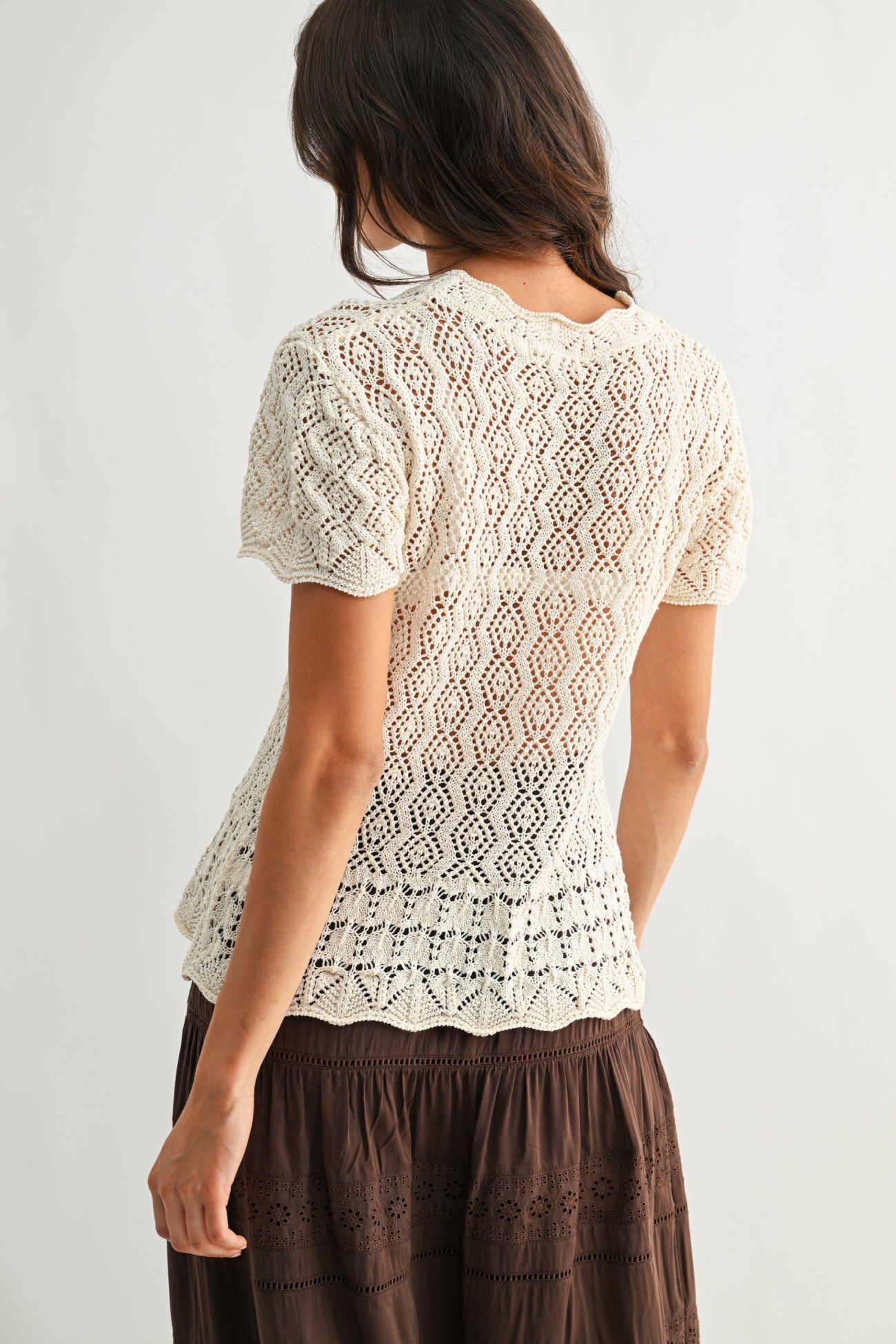 Back view of a woman wearing a cream lace top and brown skirt on a white background