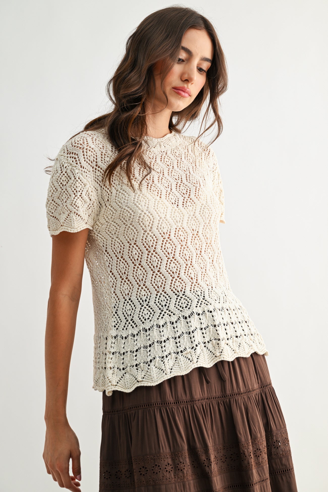 Woman wearing a cream lace top and brown skirt on a white background