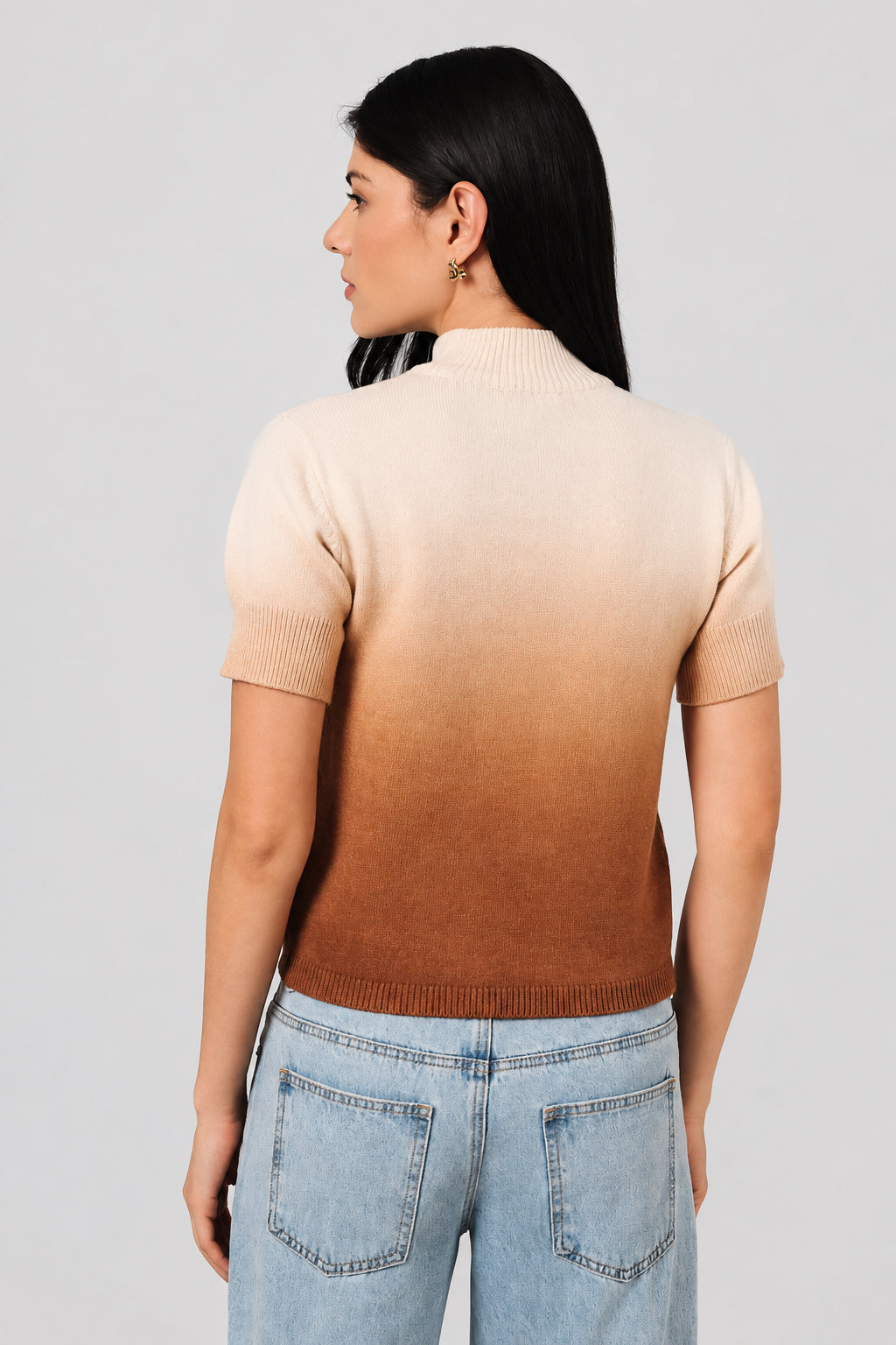 Back view of a woman wearing an ombre mock neck short sleeve sweater against a white drape background