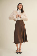 Woman wearing an espresso flare midi skirt and beige jacket on a beige background