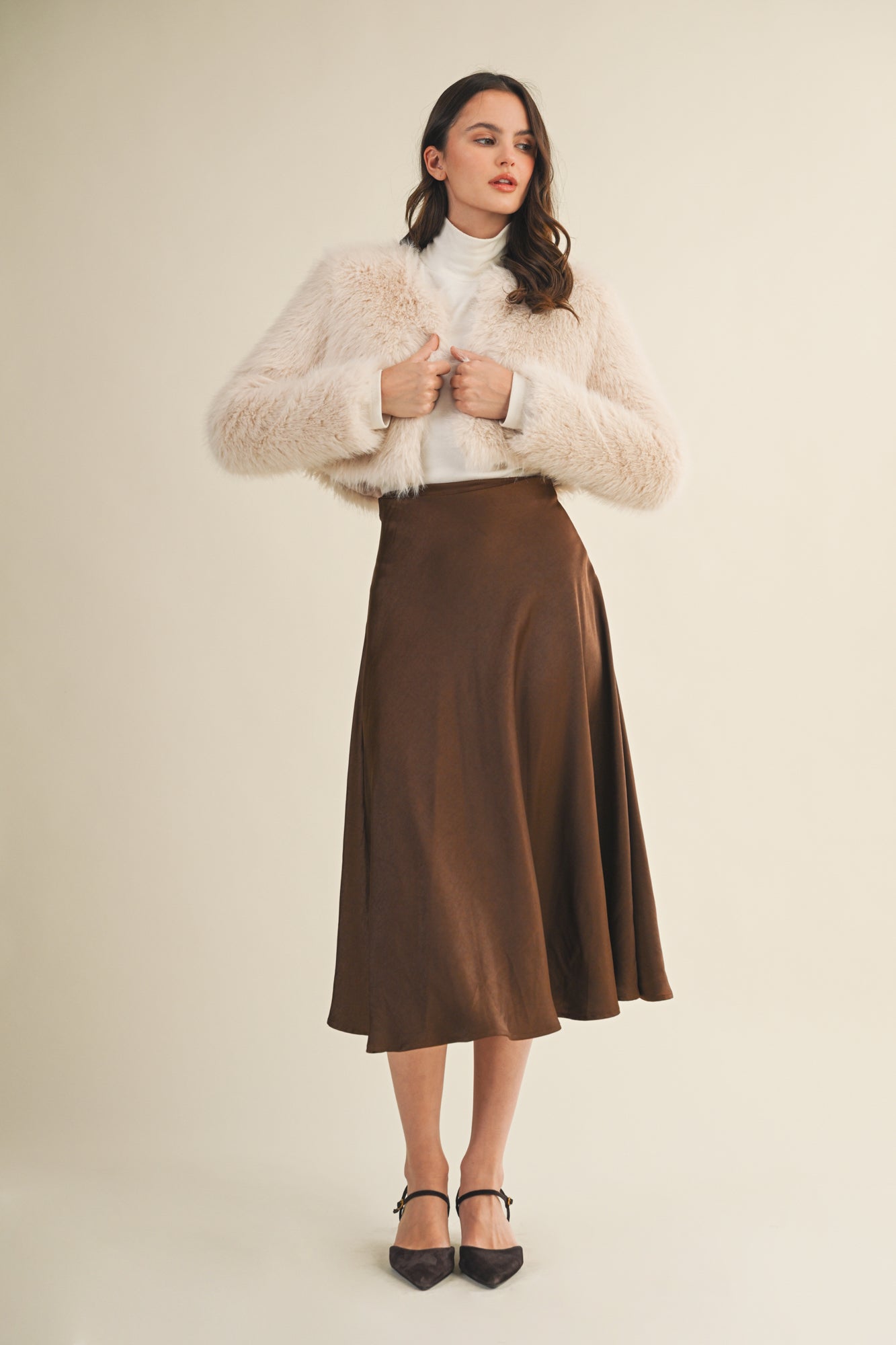 Woman wearing an espresso flare midi skirt and beige jacket on a beige background