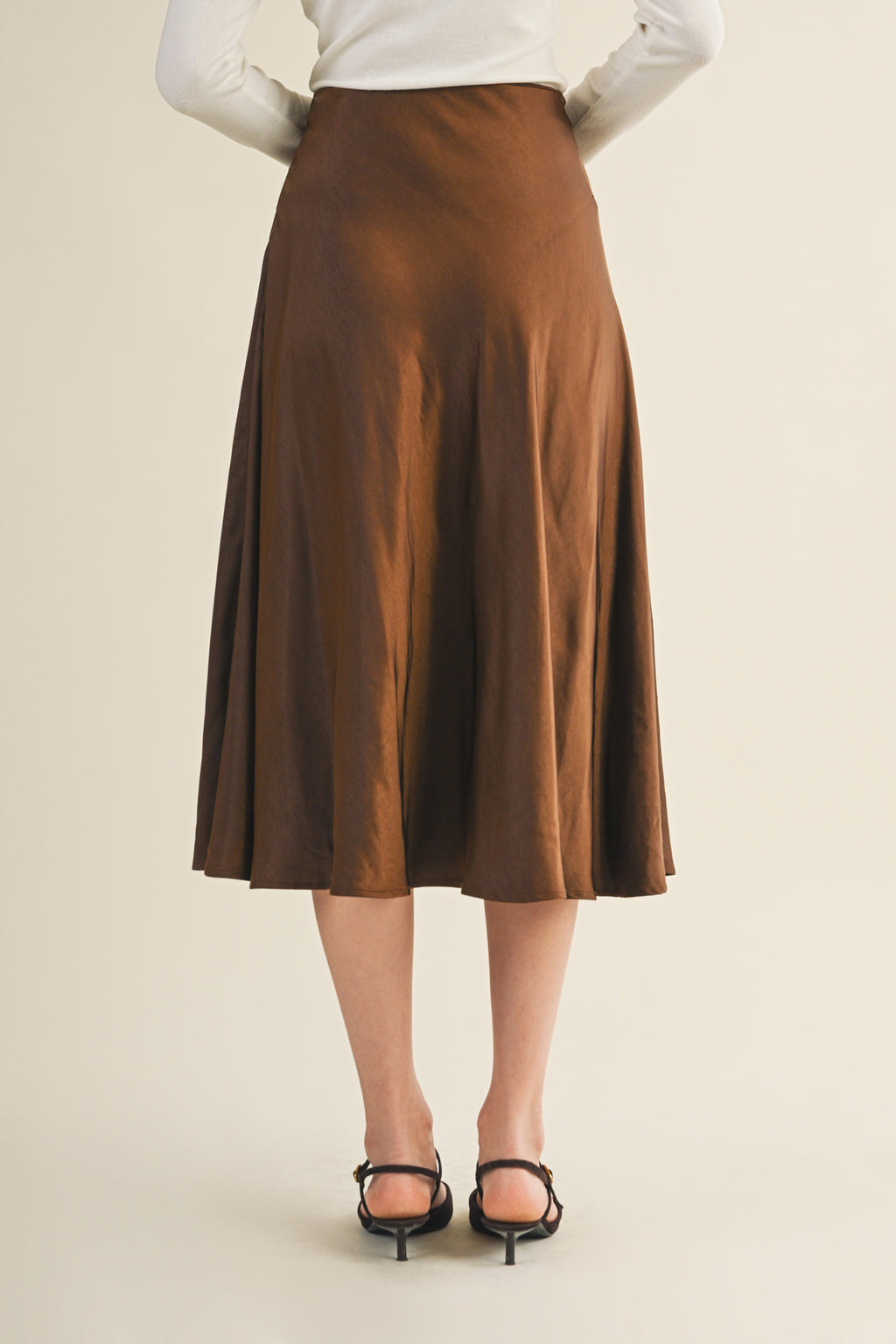 Back view of a woman wearing an espresso flare midi skirt on a beige background