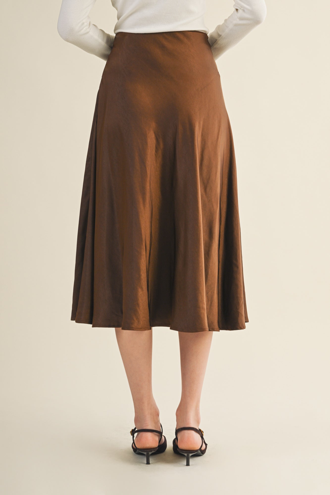 Back view of a woman wearing an espresso flare midi skirt on a beige background