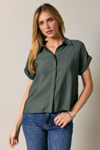 Woman wearing a green short-sleeve shirt and blue jeans against a beige background