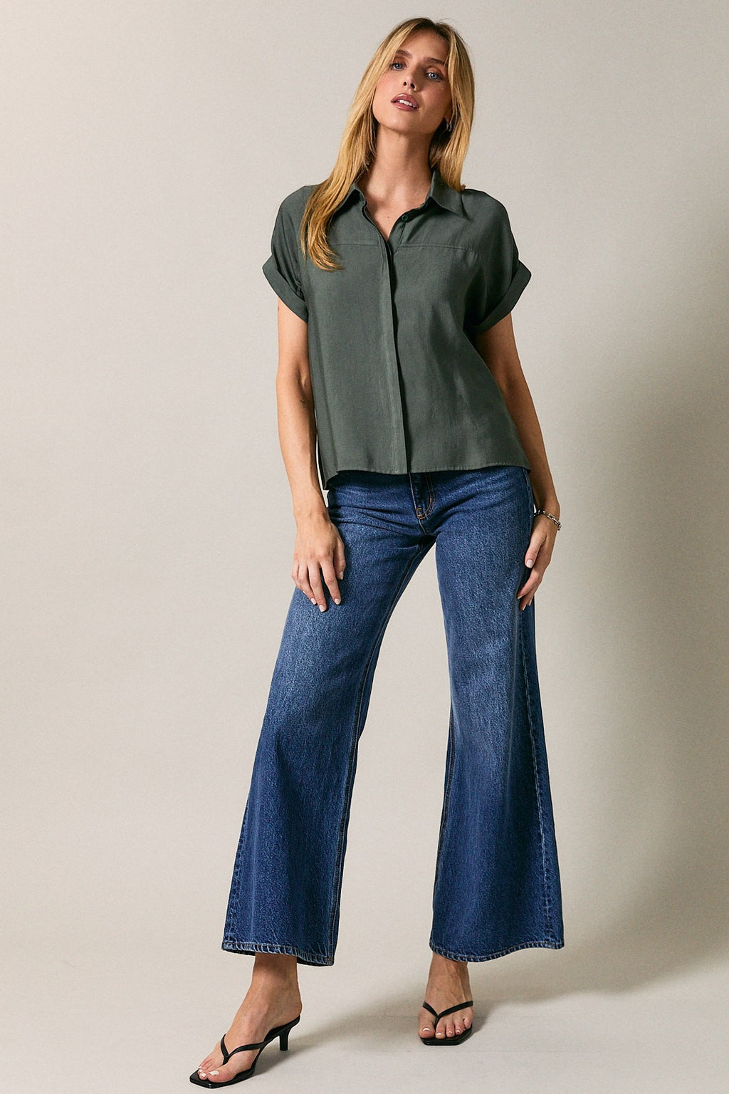 Woman wearing a green shirt and blue jeans against a plain background