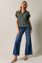 Woman wearing a green shirt and blue jeans against a plain background