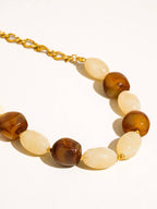 Brown and ivory beads with delicate gold tone beads and link chain on white background