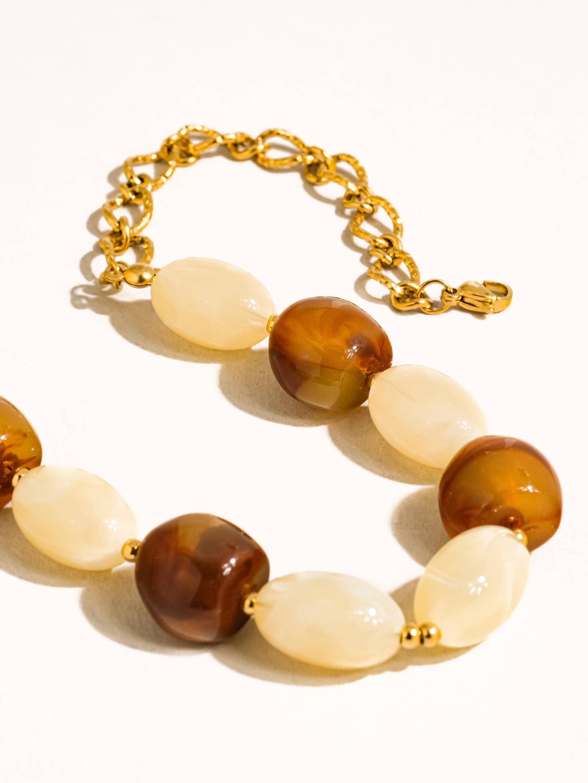 Brown and ivory beads with delicate gold tone beads and link chain on white background