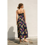 Back view of a woman wearing a navy floral dress with side slit against a light background