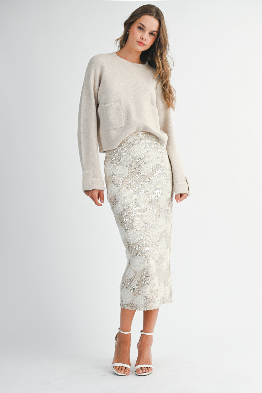 Woman wearing a light taupe sweater and white lace skirt on a white background