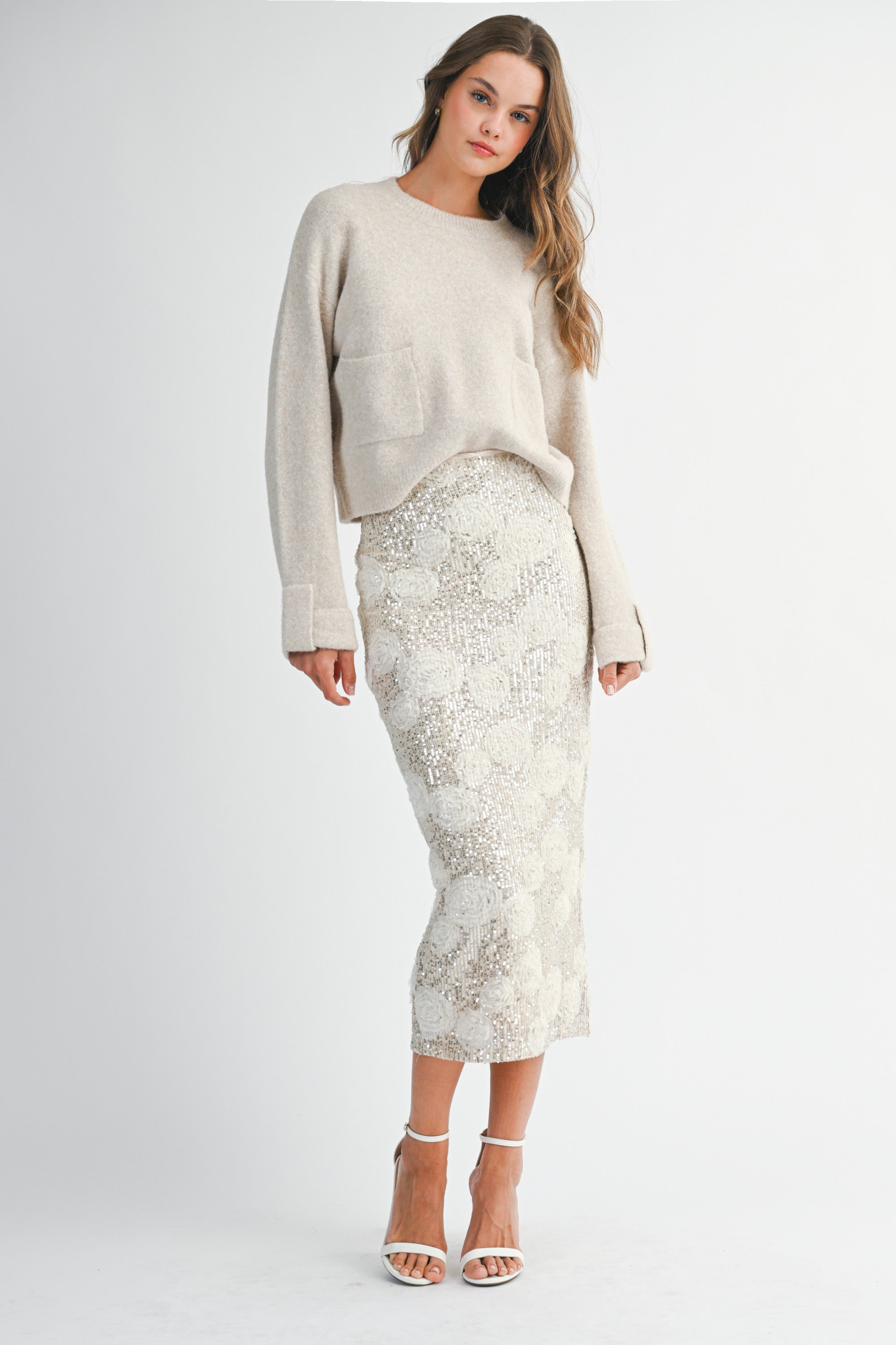 Woman wearing a light taupe sweater and white lace skirt on a white background