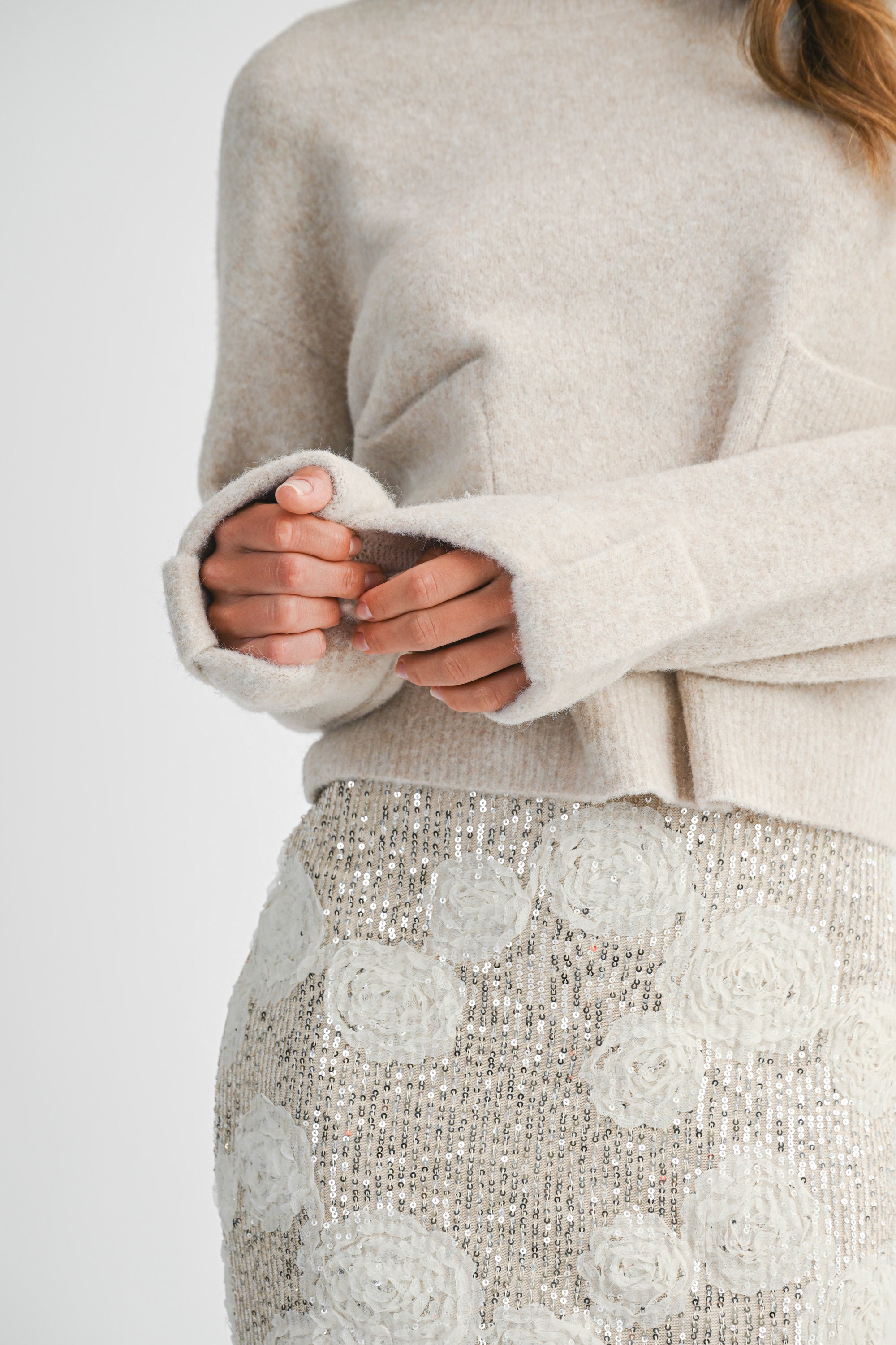 Woman wearing a light taupe sweater and white lace skirt on a white background