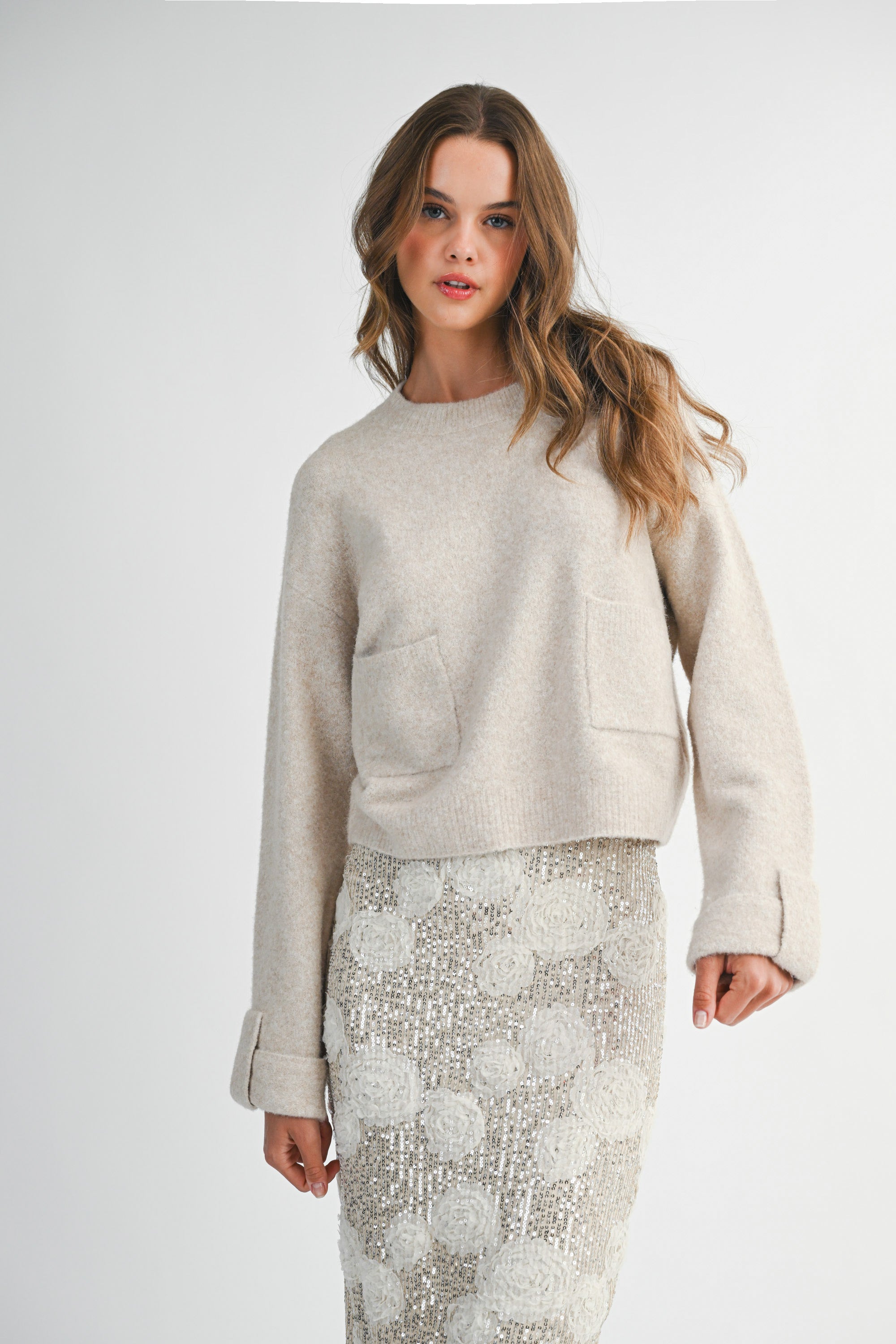 Woman wearing a light taupe sweater and white lace skirt on a white background