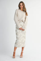 Woman wearing a light taupe sweater and white lace skirt on a white background