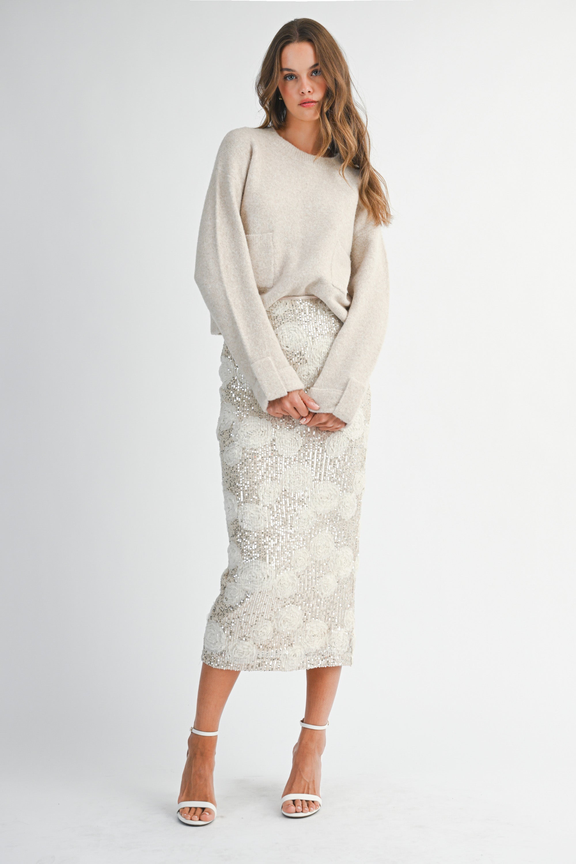 Woman wearing a light taupe sweater and white lace skirt on a white background