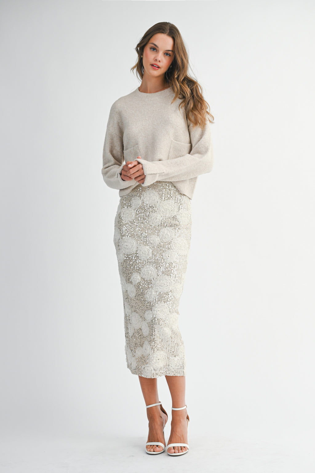 Woman wearing a light taupe sweater and white lace skirt on a white background