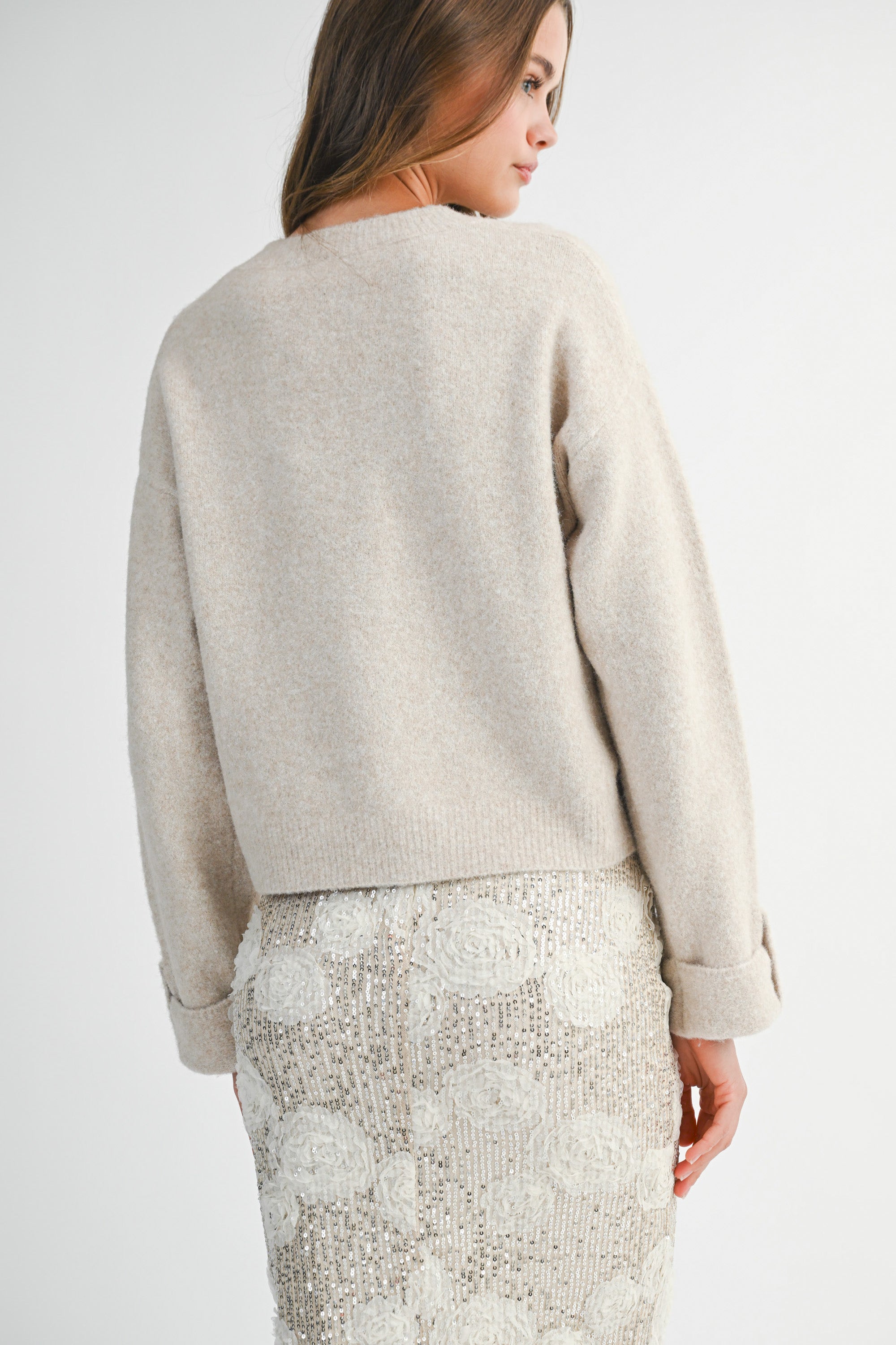 Back view of a woman wearing a light taupe sweater and white lace skirt on a white background