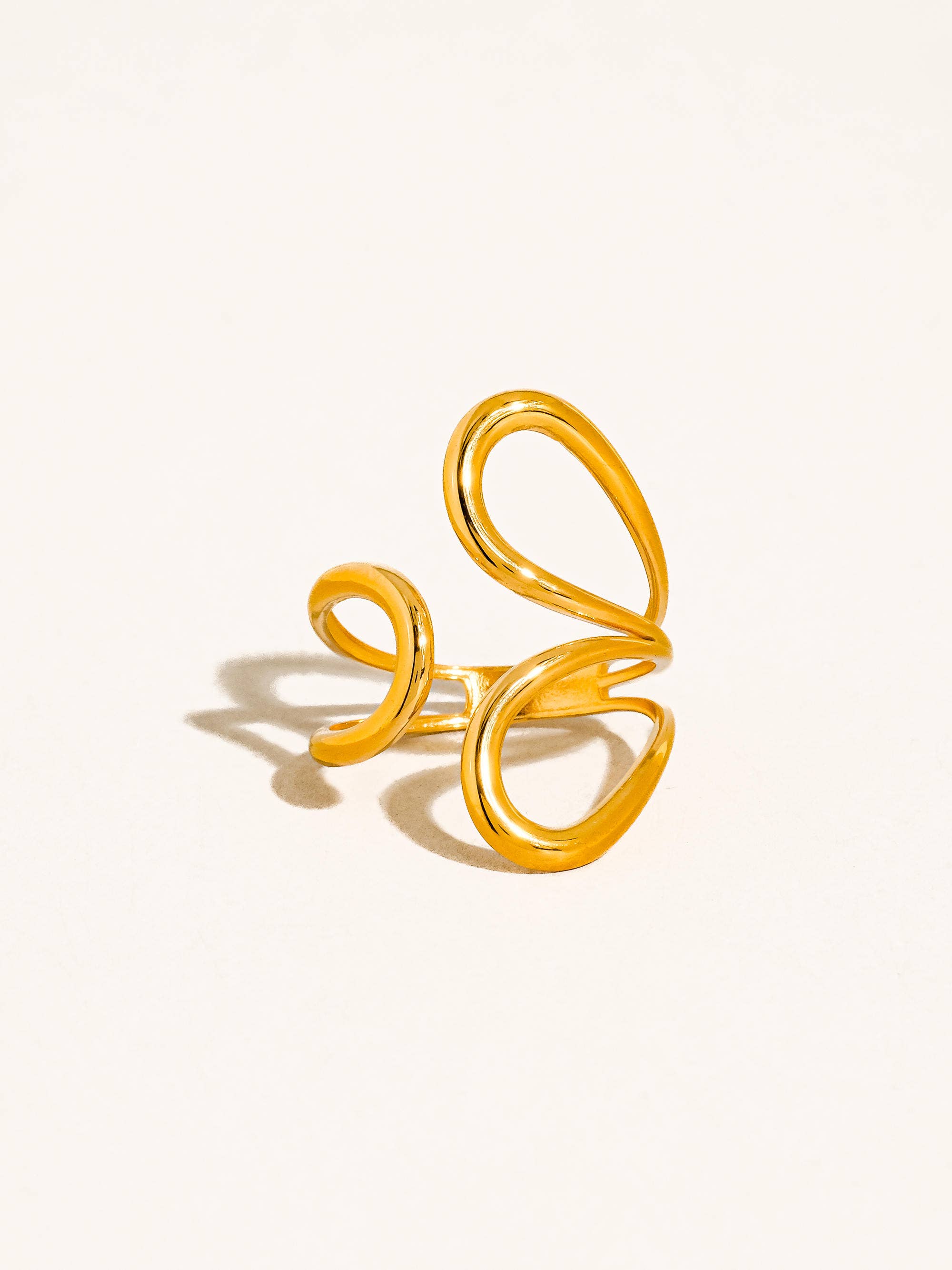 Gold open abstract swirl ring on a light beige background