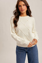 Woman wearing diamond design pearl embellishment cream sweater on gray background