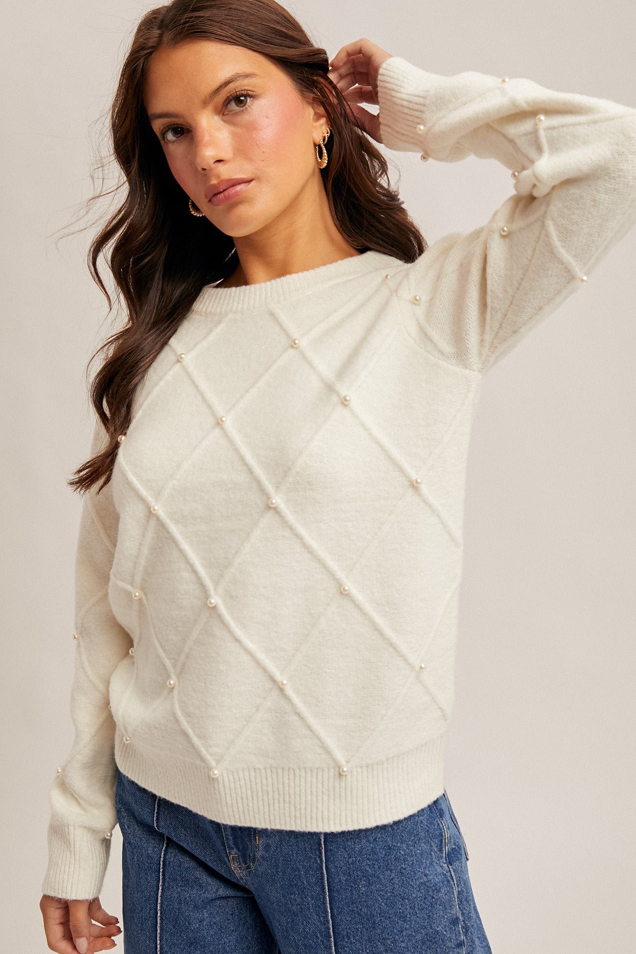 Woman wearing diamond design pearl embellishment cream sweater on gray background