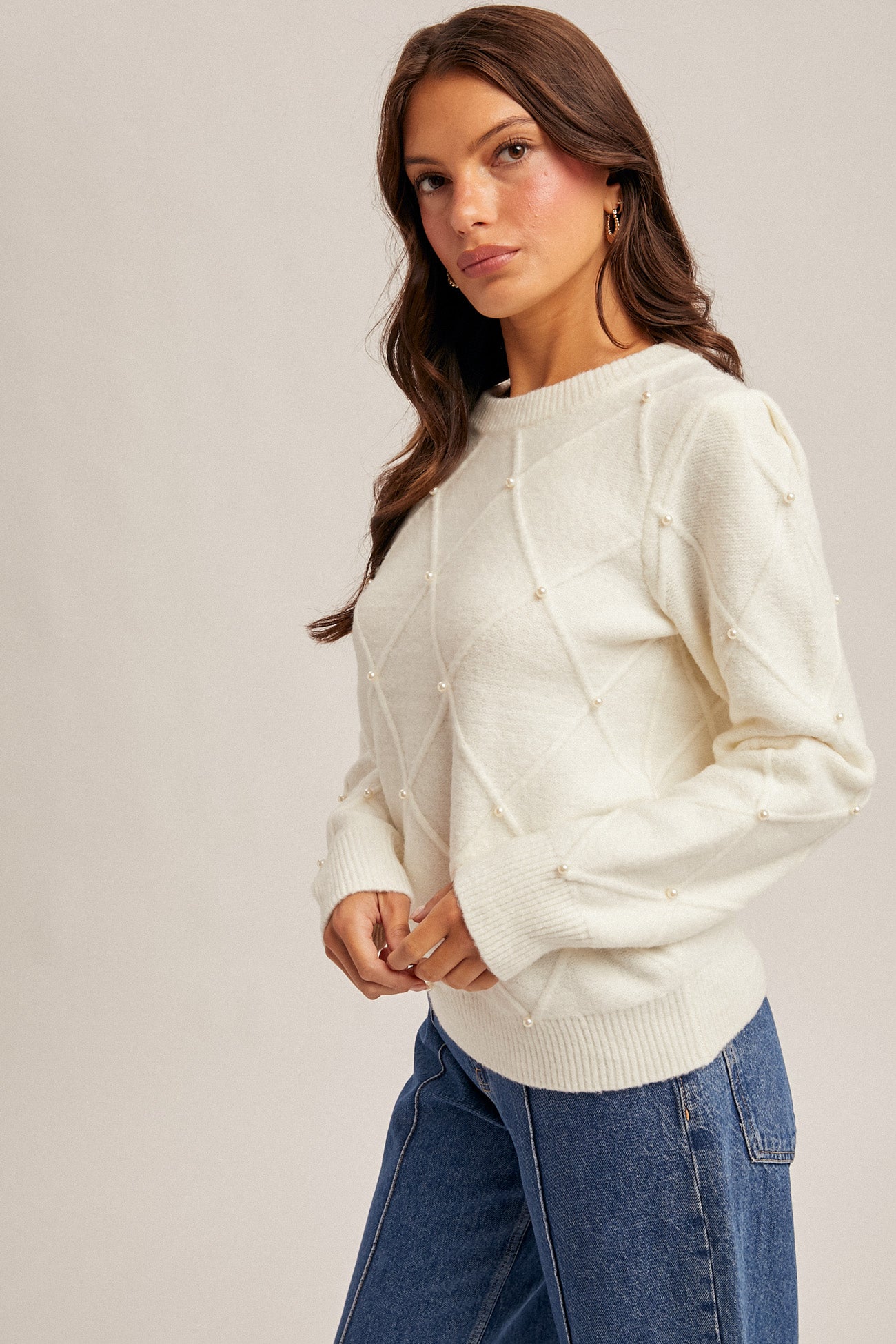 Woman wearing diamond design pearl embellishment cream sweater on gray background
