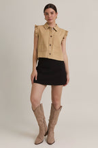 Woman wearing taupe ruffle detail button down collar jean vest with black skirt on beige  background
