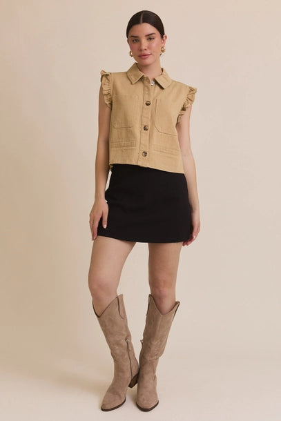 Woman wearing taupe ruffle detail button down collar jean vest with black skirt on beige  background