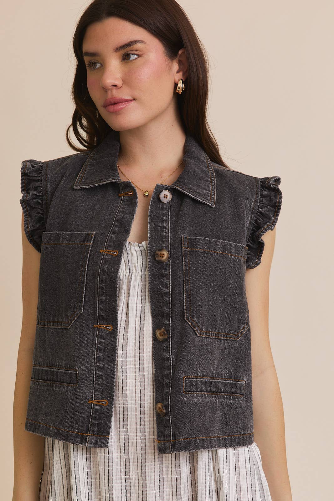 Woman wearing ruffle sleeve detail charcoal vest on striped dress on beige background