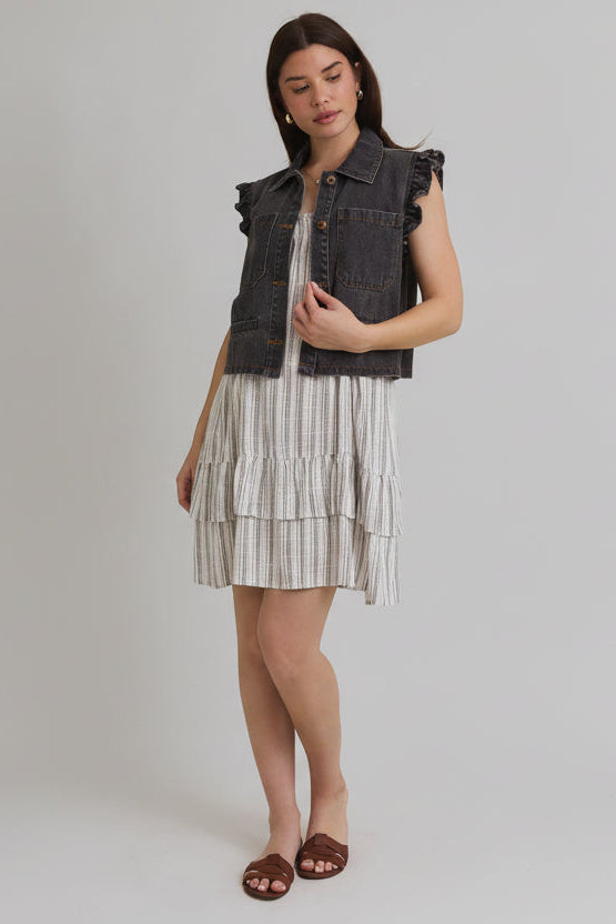 Woman wearing ruffle sleeve detail charcoal vest on striped dress on beige background
