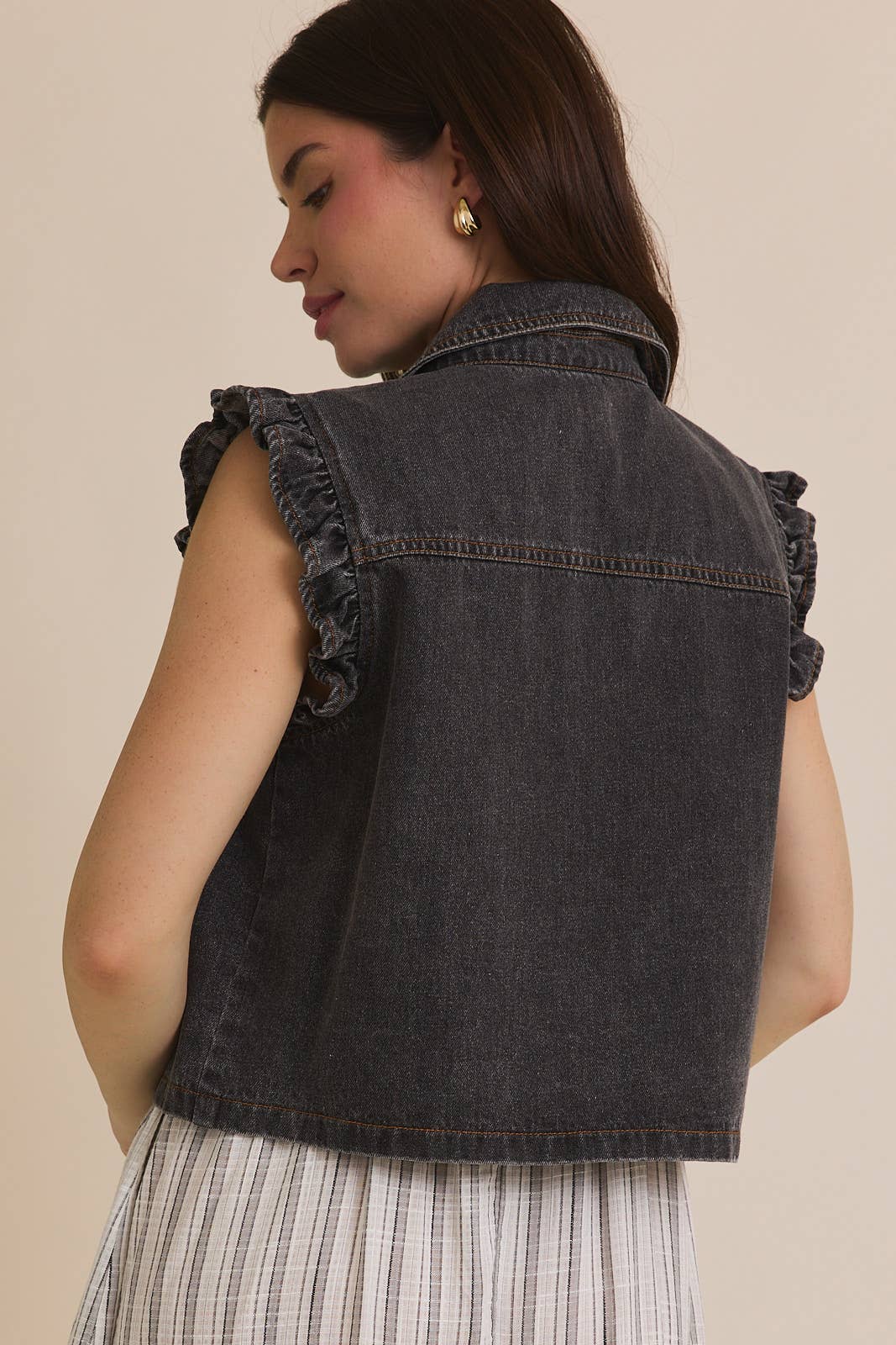 Woman wearing ruffle sleeve detail charcoal vest on striped dress on beige background