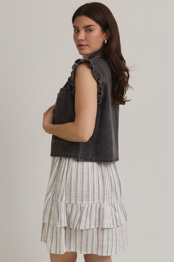 Woman wearing ruffle sleeve detail charcoal vest on striped dress on beige background