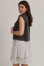 Woman wearing ruffle sleeve detail charcoal vest on striped dress on beige background