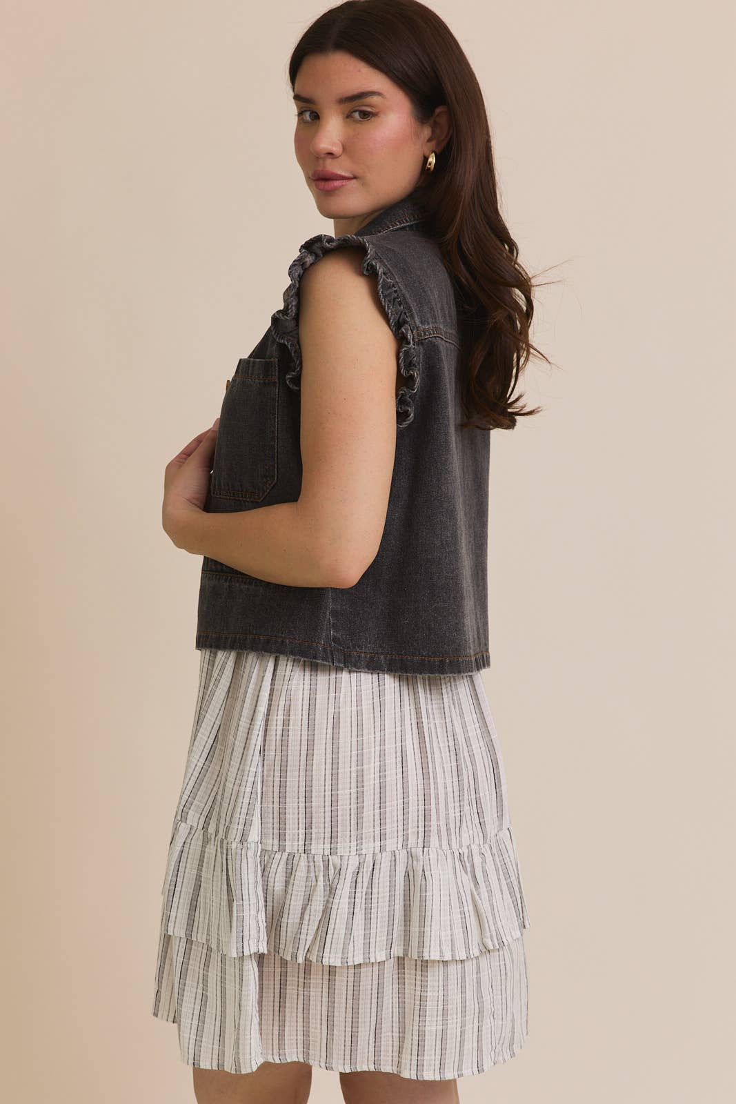 Woman wearing ruffle sleeve detail charcoal vest on striped dress on beige background