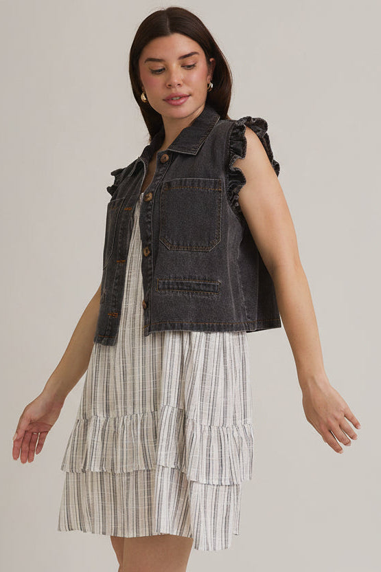 Woman wearing ruffle sleeve detail charcoal vest on striped dress on beige background