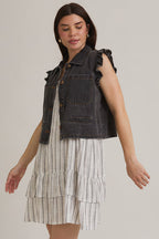 Woman wearing ruffle sleeve detail charcoal vest on striped dress on beige background