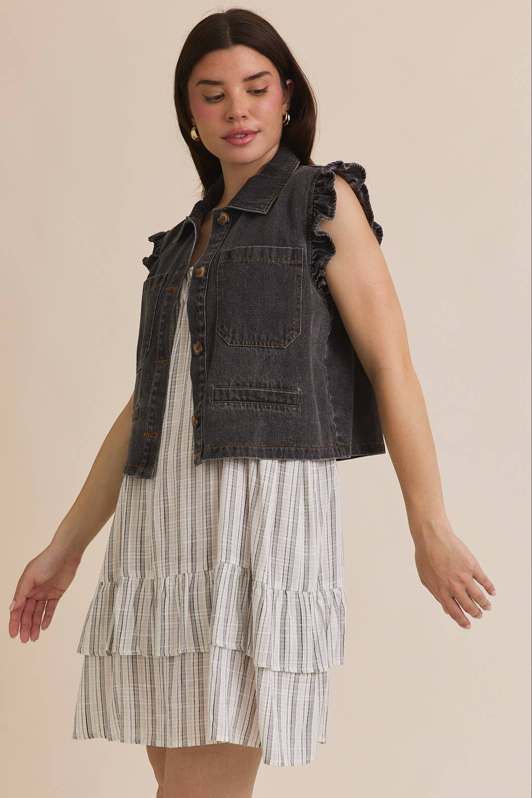 Woman wearing ruffle sleeve detail charcoal vest on striped dress on beige background