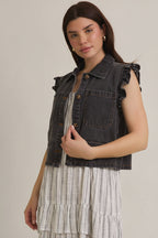 Woman wearing ruffle sleeve detail charcoal vest on striped dress on beige background
