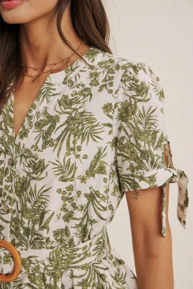 Woman wearing an olive floral dress  with tie detail short sleeve with a plain background