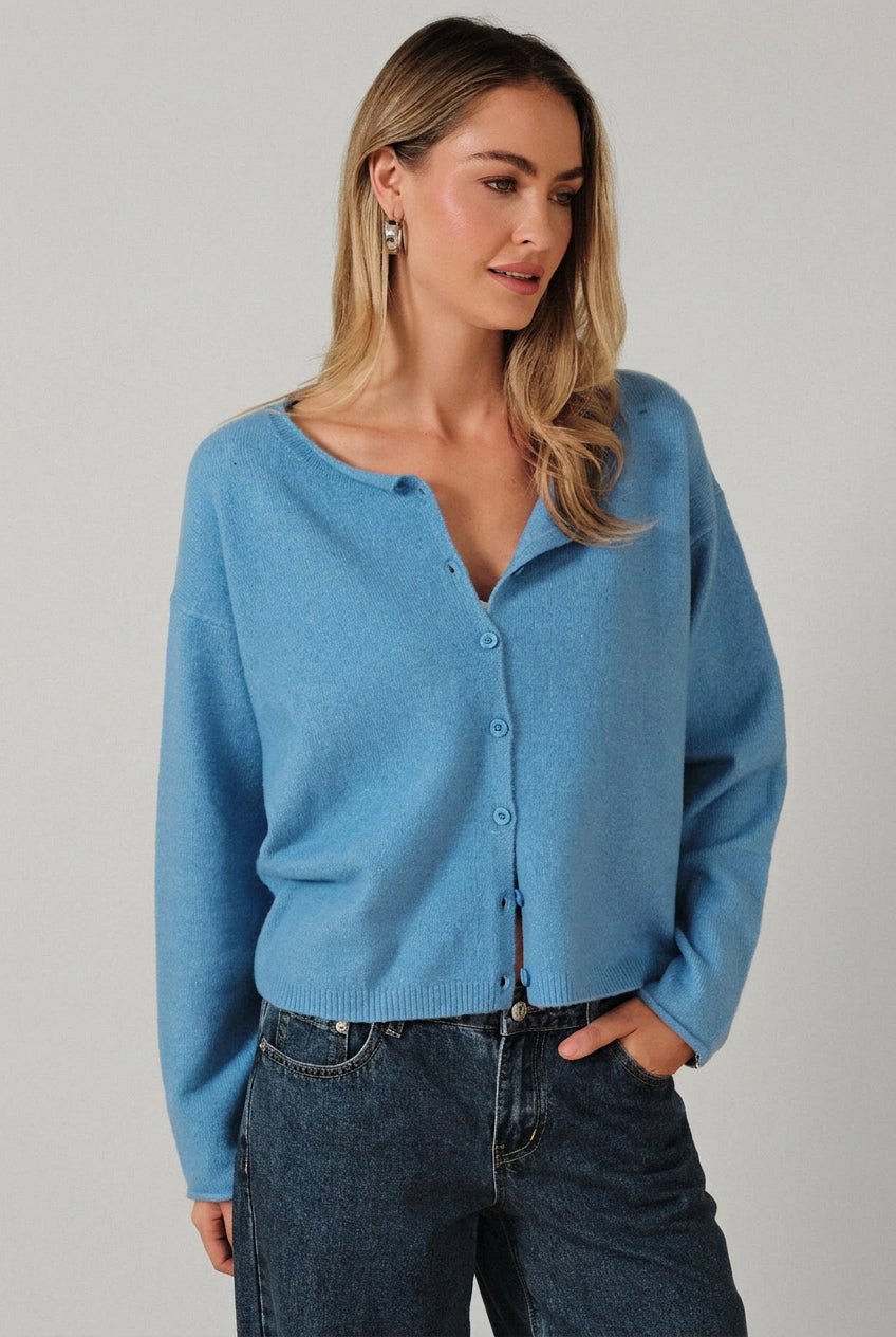 Woman wearing a blue cardigan  and jeans against a beige background