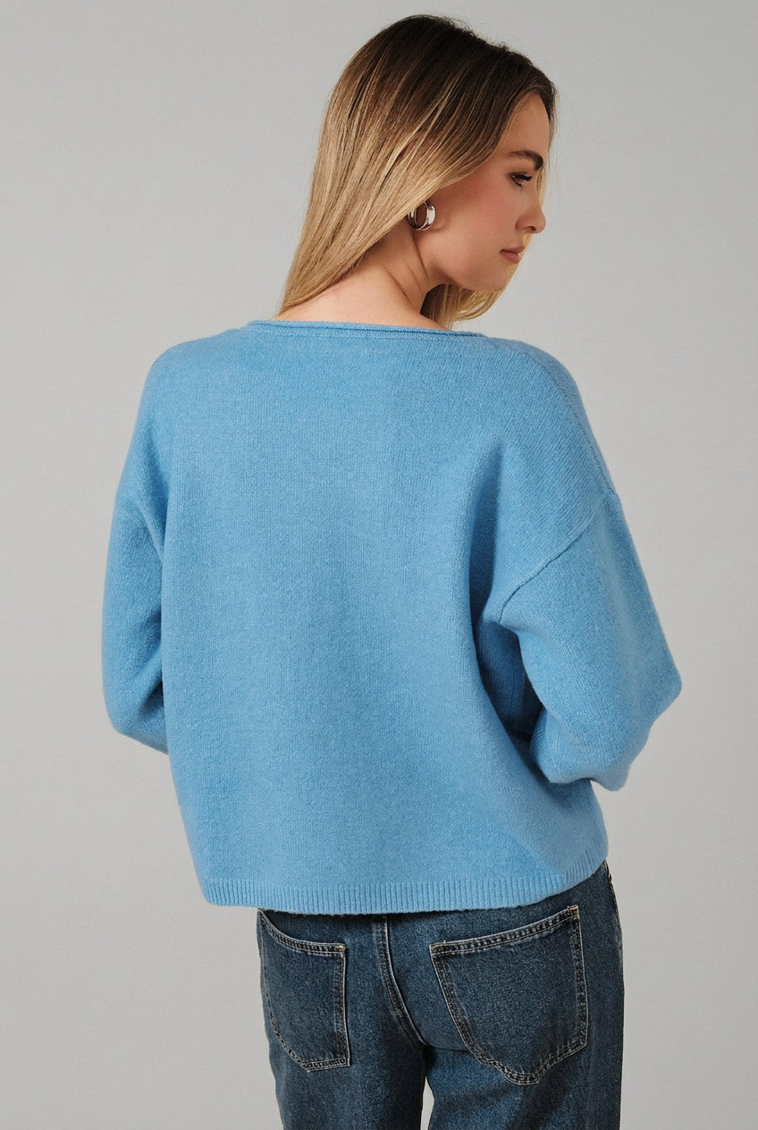 A woman shown from the back wearing a light blue knit sweater and dark blue jeans, standing against a solid beige background.